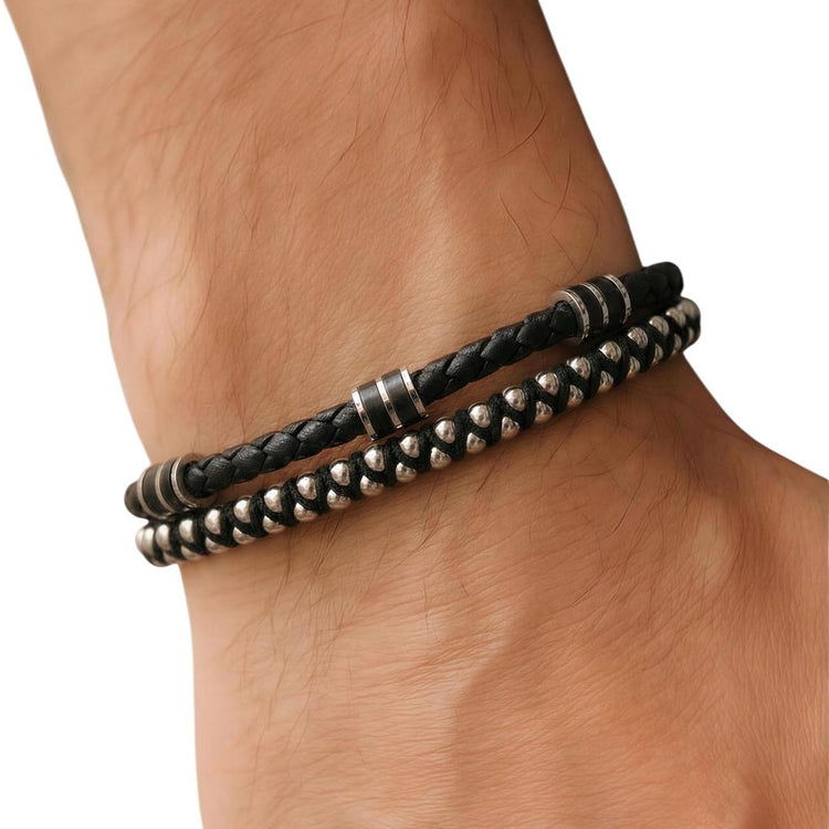 Close-up of a wrist wearing two black braided leather bracelets with metal beads on a white background.