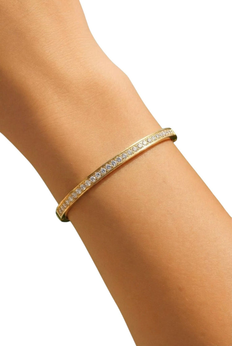 Gold bracelet with clear stones on a person's wrist against a white background
