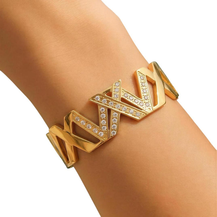 Gold bracelet with geometric design on a wrist against a white background