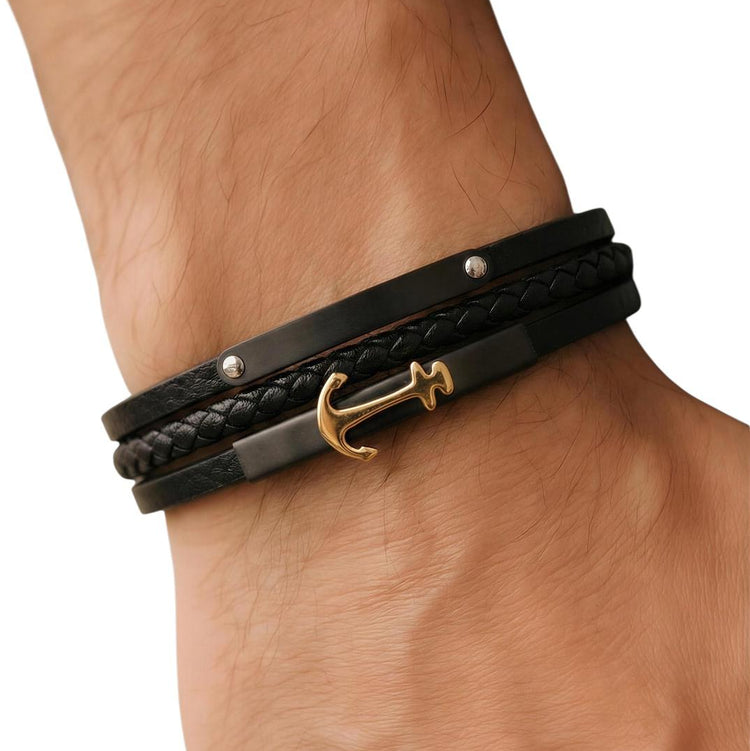 Black leather bracelet with gold anchor charm on a wrist against a white background