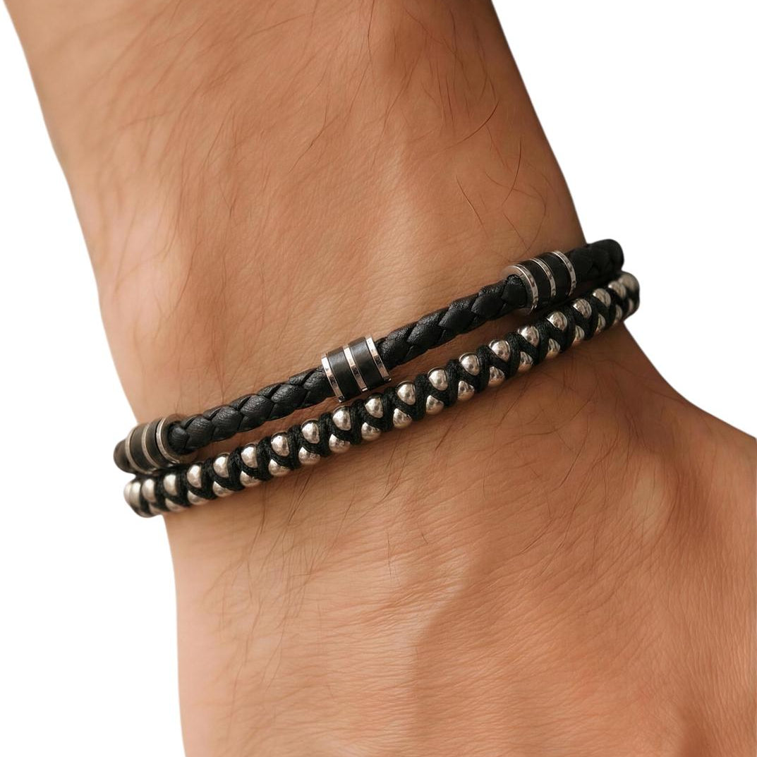 Close-up of a wrist wearing two black braided leather bracelets with metal beads on a white background.