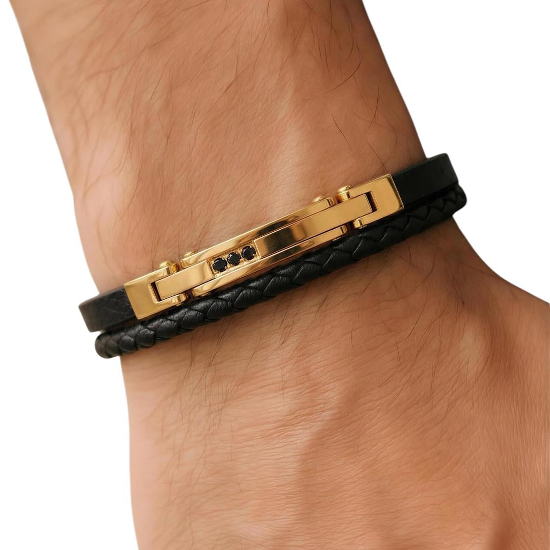 Black leather bracelet with gold accents on a wrist against a white background