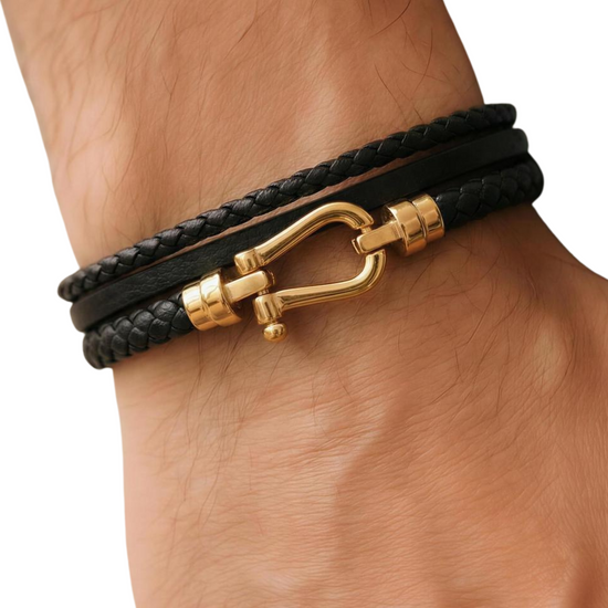 Black leather bracelet with gold clasp on a wrist against a white background