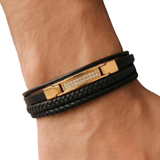 Black leather bracelet with gold clasp on a wrist against a white background