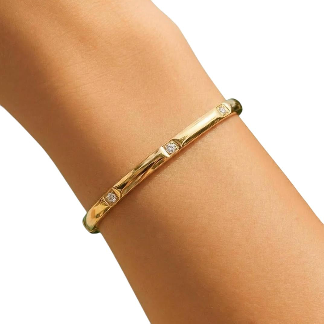 Gold bracelet with small stones on a wrist against a white background