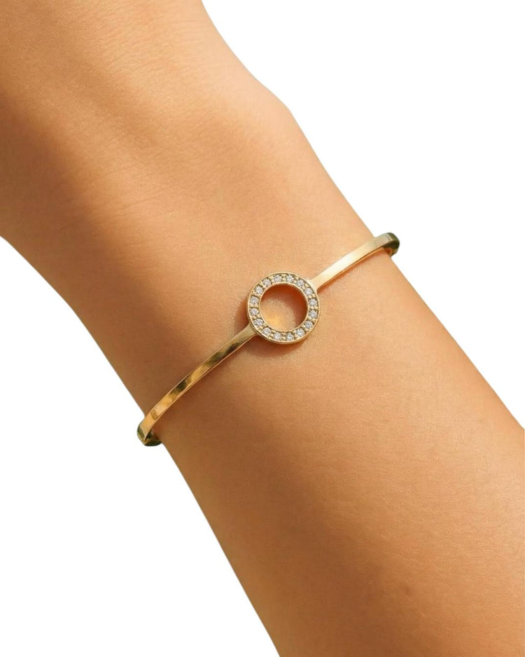 Gold bracelet with a circular design on a person's wrist against a white background